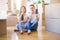 Beautiful couple sitting on the floor holding smartphone at new home around cardboard boxes serious face thinking about question,