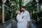 Beautiful couple in spa robes standing in hotel greenhouse, looking at each another, enjoying romantic wellness