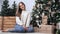 Beautiful cozy girl in casual clothing sitting near decorate christmas tree. Wide shot on RED camera