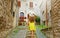 Beautiful curious young woman with yellow dress and hat goes upstairs in street in Assisi, Italy. Rear view of happy cheerful girl
