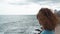 Beautiful curly brunette woman looking at the sea on a cloudy day.