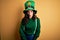 Beautiful curly hair woman wearing green hat with clover celebrating saint patricks day afraid and shocked with surprise