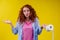 Beautiful curly redhead ginger woman holding eco toilet paper roll on yellow color background