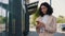 Beautiful curly smiling young businesswoman in formal outfit standing near the business centre using smartphone. People