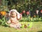 Beautiful and cute caucasian baby girl with headband bunny ears sits on the lawn with flowers.