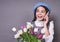 Beautiful cute Caucasian lady in a stylish blue hat in a beret with a phone holds tulips flowers in her hands on a gray background