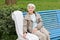 Beautiful cute elderly woman sitting on park bench blue