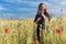 Beautiful cute girl with big lips and red lipstick in a black jacket with a flower poppy standing in a poppy field at sunset