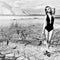 Beautiful cute girl in a fashion shoot in a bathing suit in desert dry cracked earth in the background of the mountains
