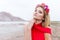 Beautiful cute girl with long blond hair in a long red evening dress with a wreath of roses and orchids in her hair standing