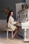 Beautiful cute girl in white warm jacket at home playing on old piano