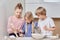 Beautiful cute kids blond siblings helping mom in the kitchen.