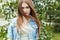 Beautiful cute sweet girl with long red hair and green eyes in a denim jacket near a flowering tree in the park the wind