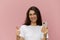 beautiful cute woman with a trendy phone in her hands stands on a pink background in a white t-shirt, holds her thumb up