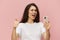 beautiful cute woman with a trendy phone in her hands stands on a pink background in a white t-shirt, holds her thumb up