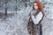 Beautiful cute young girl with red hair walking in a snowy forest among the trees missed first trimester bushes with red