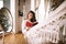 Beautiful dark-haired girl dressed in pants and sweater reads a book lying in a hammock next to the round mirror on the