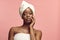 Beautiful dark skin woman wearing in body and head towel standing on a pink background touching self face.