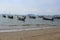 Beautiful day shot of rows of long boats in shallow ocean waters by the shore of yellow sand beach with islands, hills and