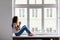 Beautiful daydreamer. Beautiful young woman holding coffee cup with smile while sitting at windowsill at home