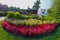 Beautiful decorative flowerbed with small red flowers and green shrubs against the background of a lake with fountains