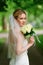 Beautiful and delicate bride in veil and with a bouquet of white roses.