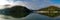Beautiful early morning panoramic view of a creek with reflections of blue sky, boats, foggy mountains and trees on water