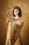 Beautiful Egyptian woman like Cleopatra pointing finger away on golden background