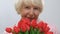 Beautiful elderly woman sniffing bunch of tulips and smiling at camera, holiday