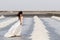 Beautiful and elegant bride with long white dress walking in salt field surrounded by heaps of salt, carrying traditional baskets