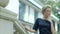 Beautiful elegant caucasian woman in a black dress walking up the stairs outside the building.