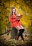 Beautiful elegant girl with orange coat reading sitting on a stump autumnal park. Young pretty woman with blonde hair reading