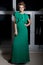 Beautiful elegant long-legged girl in a long green evening dress with evening hairstyle and bright make-up, new year\'s evenin