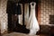 Beautiful and elegant white wedding dress and man groom wedding suite hanging on a wardrobe in anticipation of the celebration of