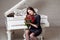 Beautiful emotional brunette woman in black classic dress holding bouquet of red roses sitting near piano with closed eyes,