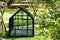 Beautiful empty Glass greenhouse in a serene, quaint back yard surrounded by evergreen trees, used for a home gardening hobby by a