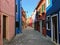 A beautiful empty narrow shaded cobblestone street with an array of old colourful square homes on the small island of Burano