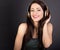 Beautiful enjoying toothy smiling young woman listening the music in wireless headphone with closed eyes on dark grey background.