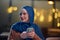 A beautiful European Muslim woman, adorned with a hijab, utilizes her smartphone to swiftly prepare for iftar during the