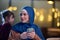 A beautiful European Muslim woman, adorned with a hijab, utilizes her smartphone to swiftly prepare for iftar during the