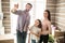 Beautiful family is standing together in their new apartment. Man is looking straight and pointing. His wife and
