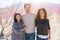 Beautiful family of three smiling cheerful walking toghether on peach garden with pink petals enjoying sunny day of spring