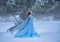 Beautiful fantasy woman in a medieval blue lush dress walks in winter forest. Vintage historical clothing flies in wind