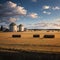 a beautiful farmer\\\'s field and grain silos with hay bales.