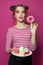 Beautiful fashion model woman holding plate with dessert sweets snacks and showing donut on vivid pink background