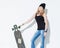 Beautiful fashionable bright young girl in jeans, a black T-shirt and hat posing with a cool longboard in the hands