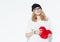 Beautiful fashionable cheerful young girl in white sweater holding a big red heart and posing near the white wall. in the studio