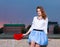 Beautiful fashionable Girl with red heart in the park in warm summer evening sitting on a stone bank of the river