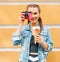 Beautiful fashionable young girl posing in a summer dress and denim jacket with pink vintage camera and multi-colored ice cream.