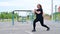 A beautiful fat girl in a black tracksuit is doing fitness exercise on the sports ground. Young woman lunges outdoors on